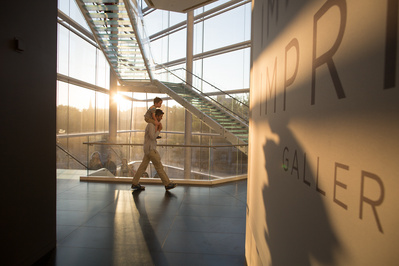 A guy with a kid on his shoulders through the MMoCA while the sun is setting behind him. 