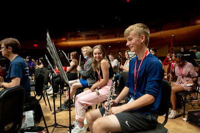 Student musicians are getting ready to play a concert as a girl smiles for the camera. 