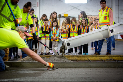 A group of girl scouts are watching cement being poured. 