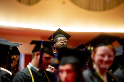 A graduate peers over some other people to get a good view of the graduation that is being held at the Monona Terrace. 