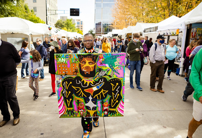 At Art Fair on the Square in Madison, Wi an artist poses with his art in the middle of the street. 
