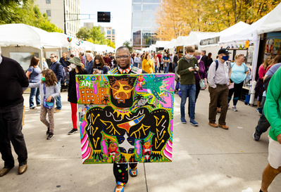 At Art Fair on the Square in Madison, Wi an artist poses with his art in the middle of the street. 