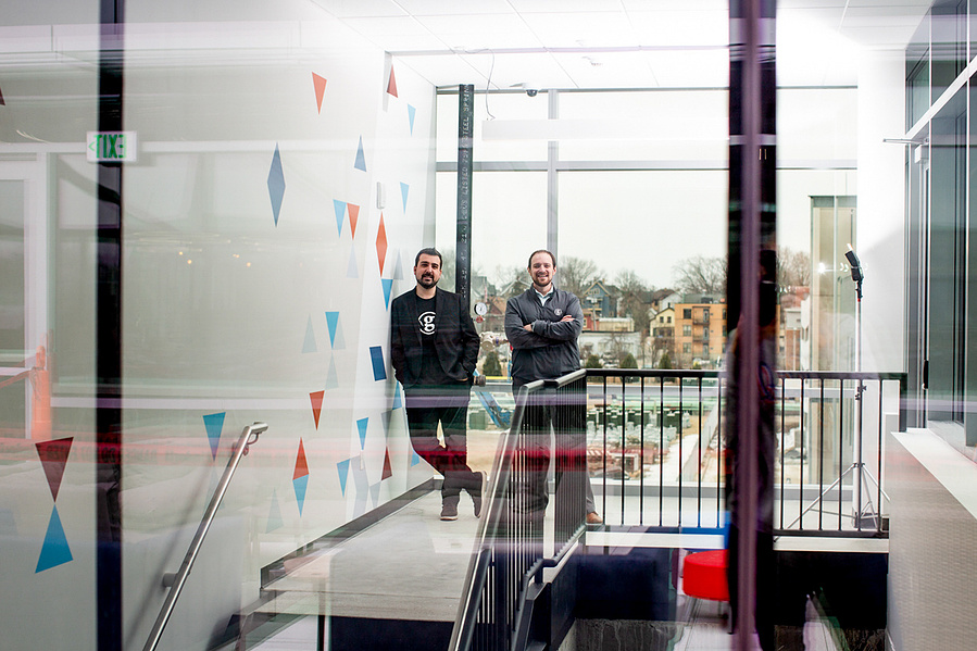 Two guys are standing behind 2 panes of glass. This is definitely a photo of start up guys--this is how I would photo start up guys. 