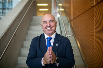 A bald and smiling man is holding his hands together and looking at the camera. 