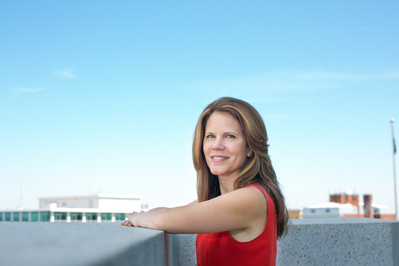 A political stands on the top of the Wisconsin State Capitol wearing a red dress. 
