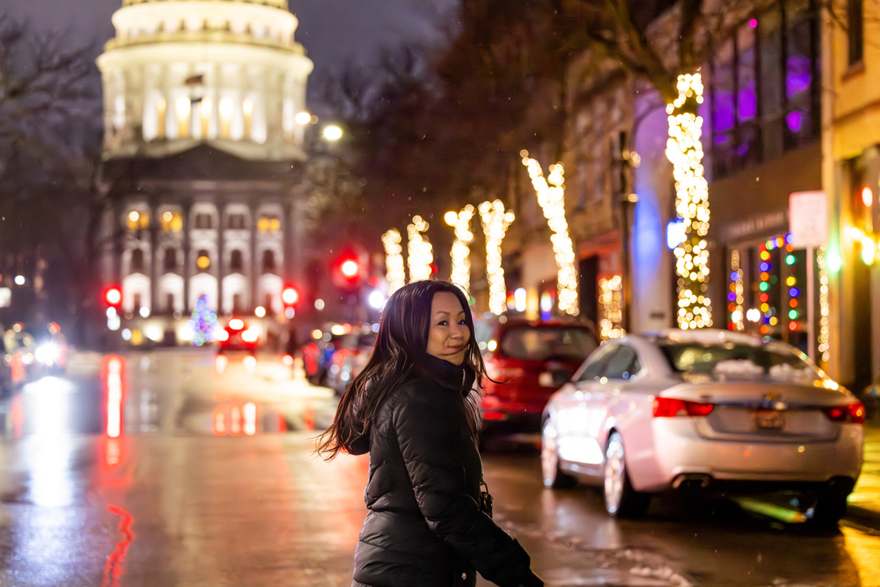A bright image where the State Capitol Building glows behind a woman lit by a wet street. The light is very dynamic in this tourism photograph.