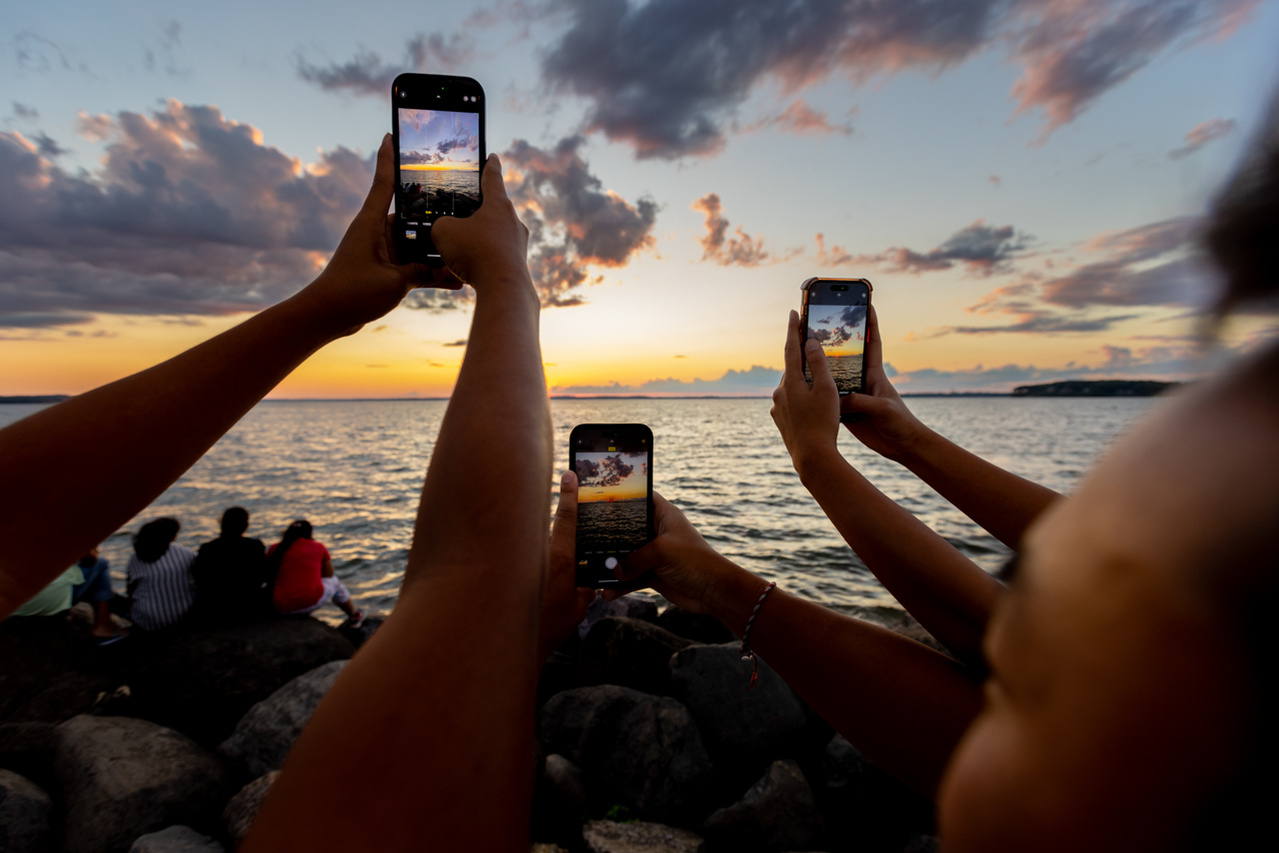 A group of students use their cell phones to take pictures of the sunset in this  website photograph at the Memorial Union on the campus of the University of Wisconsin, Madison.