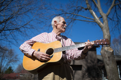 photo of Bill Malone, author of Country Music USA, is holding a guitar. 