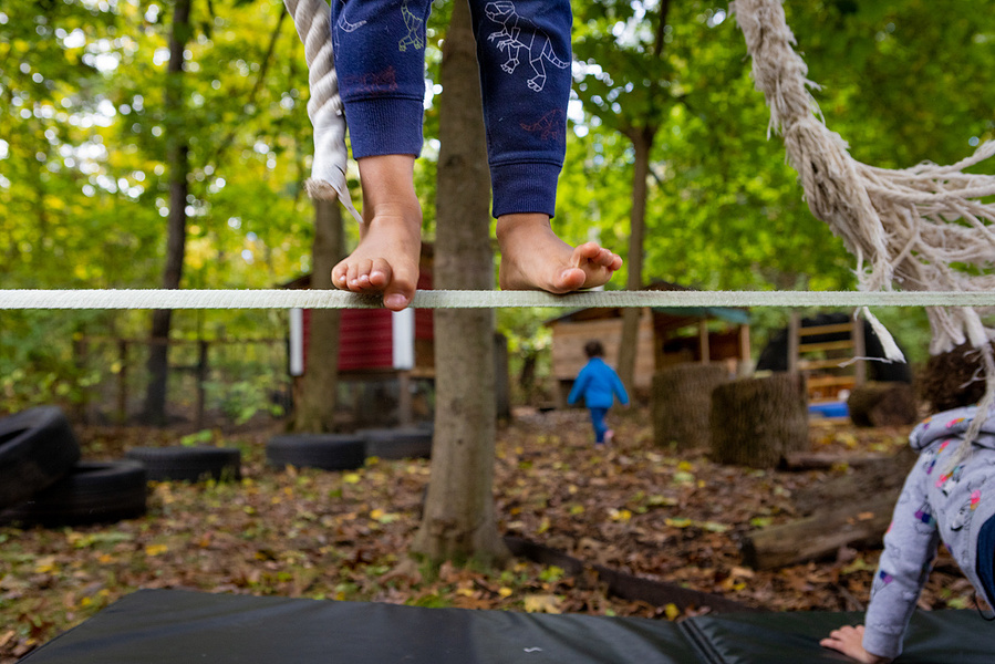 A kid balances on a rope tightrope with bare feet. One little pinky toe is raised. 