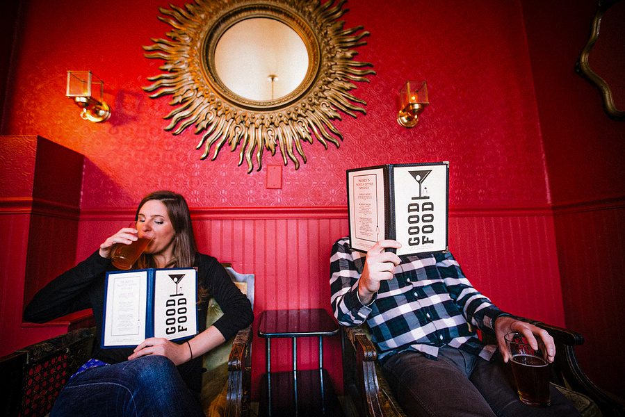 A couple is at Mickeys Bar on Willy Street in Madison, WI. They are reading the menus while drinking beers. 