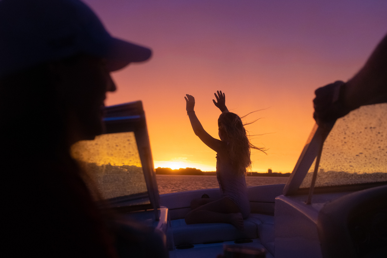 A candid portrait of a family enjoying boating on Lake Monona in Madison Wisconsin. The sunsets behind a girl celebrating Summer with her hands up.  Documentary photography of a family spending quality time together.