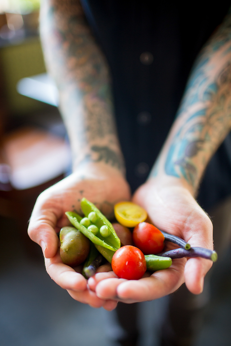 A chef with a lot of tattoos on her arms hold  fresh vegetables in her hands.