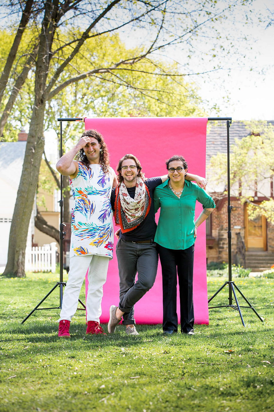 Three people stand in front a pink backdrop in a park. 