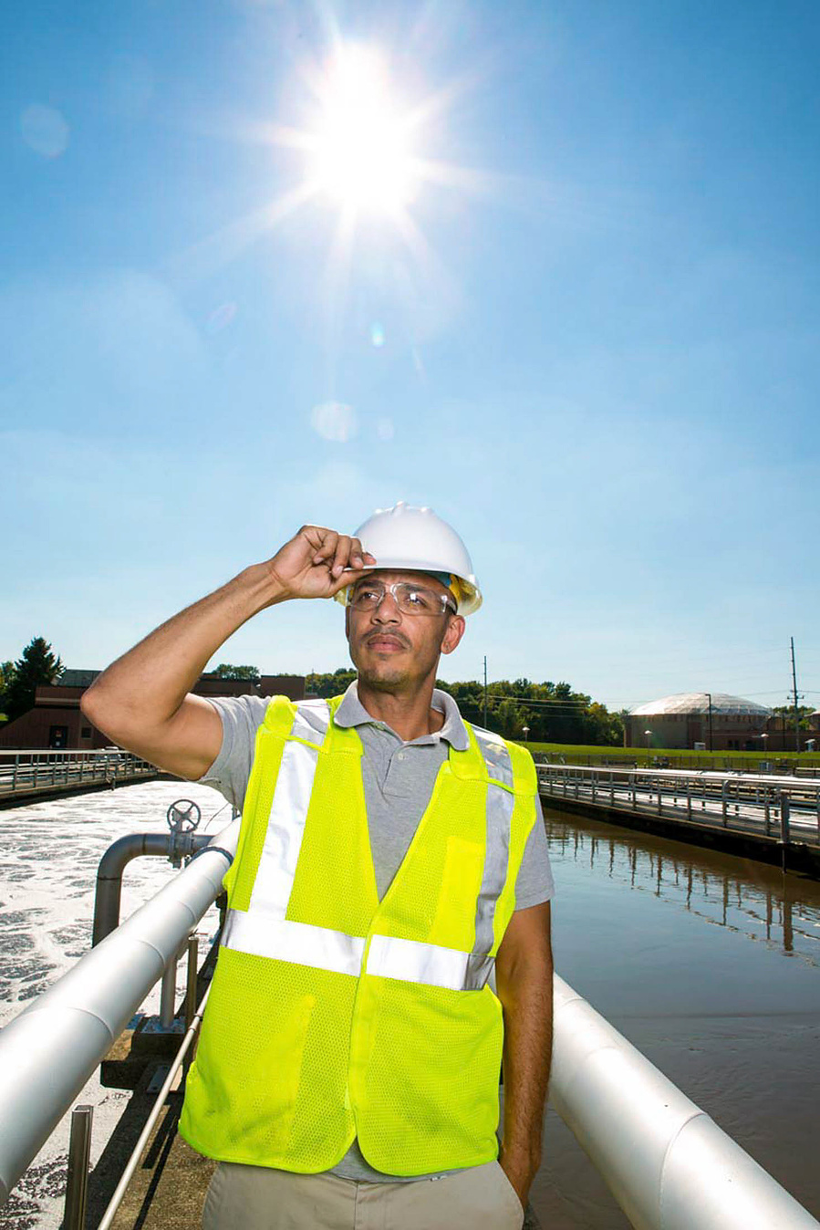 A guy at the Madison Metropolitan Sewerage District is holding his hard hat and the bright sun is right behind him. 