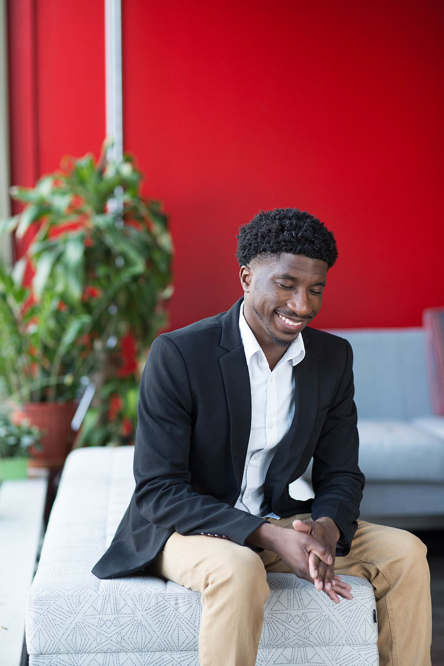 A student sits on a couch with a red wall behind him. 