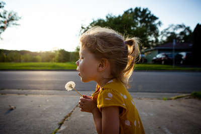 Beautiful lighting in this photo of a girl blowing the seeds off of a dandelion.