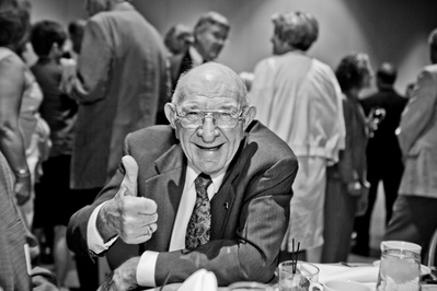 An older gentleman is smiling really big and giving a thumbs up. This will make everyone happy. 