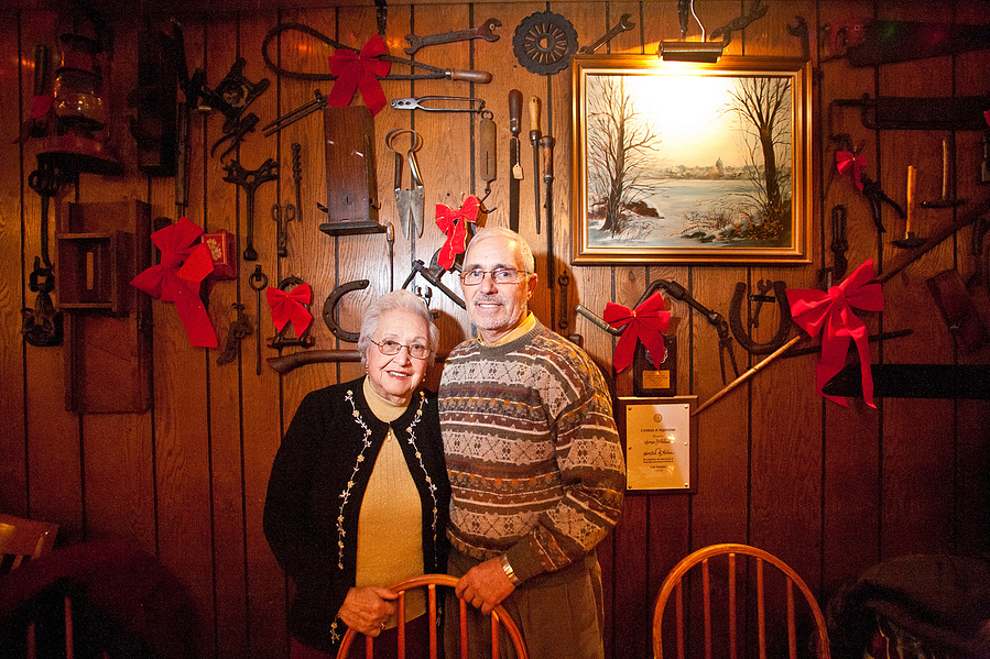 An older couple poses in front of a wall of tools that have Christmas bows on the tools. This photo cracks me up. 