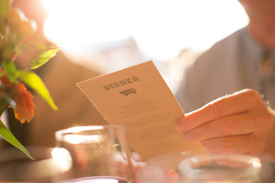 A person is holding a menu at an outdoor dinner, the sun is setting behind them making an orange hue over the whole photo. 