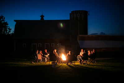 A dusk lit documentary photo of a family gathered around a fire.