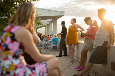 A crowd is gathered while the sun is setting on the roof of the Madison Museum of Contemporary Art. 