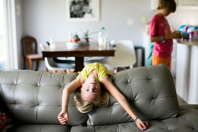 Family documentary candid photo of a child looking over a couch in their home.