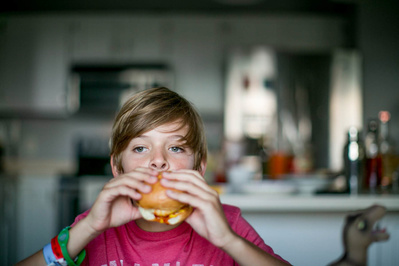 a young child enjoys a cheeseburger in this family photo. an artistic blurred background highlights the image of the kid