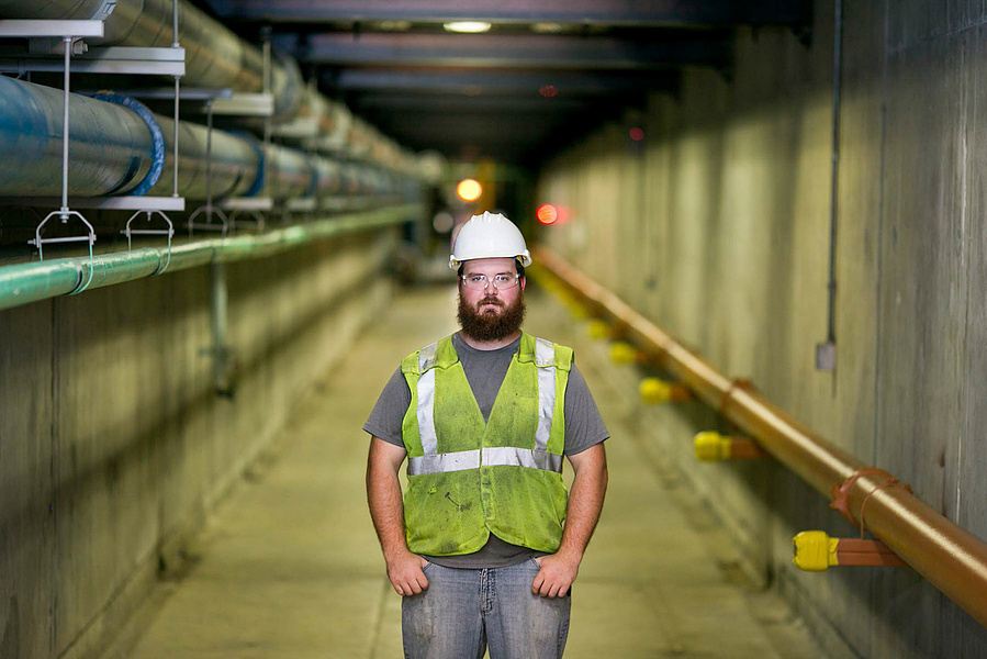 A bearded guy wearing a hard had and neon vest is posed in the tunnels at the Madison Metropolitan Sewerage District. 