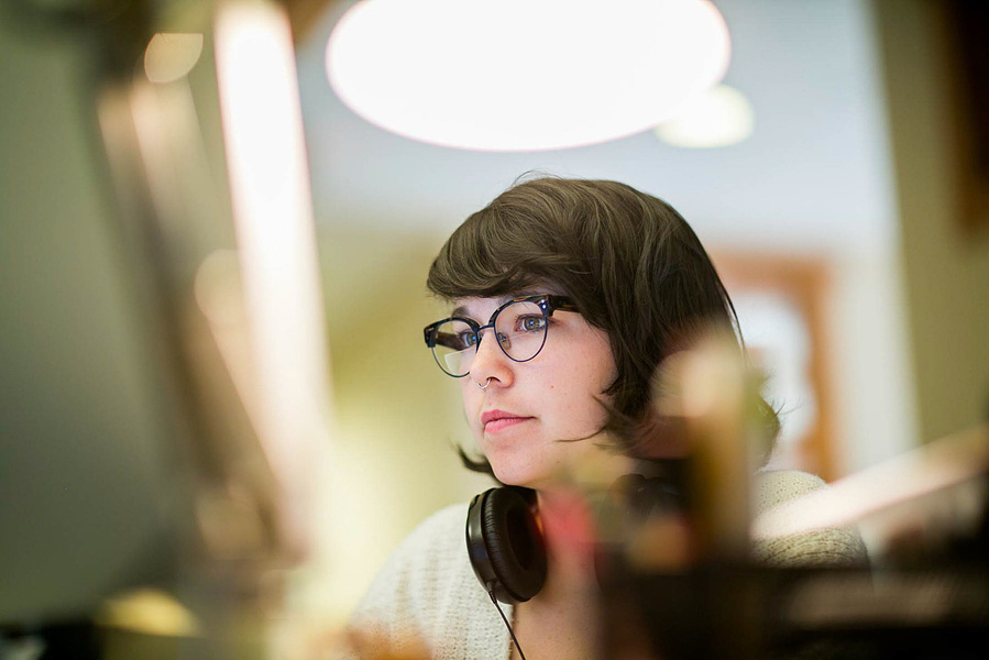 A women works on a computer at the office with headphones around her neck. 