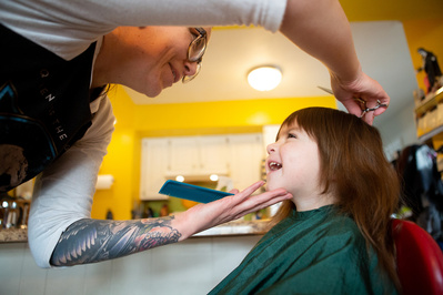 family documentary photo of a mother cutting her daughters hair with a scissors.