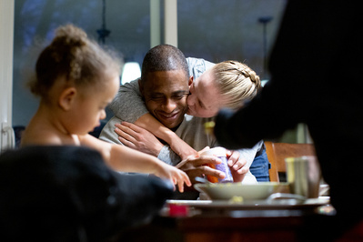 mother and father share a kissing embrace in this candid photo in the family kitchen