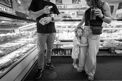 Family documentary photo of a family in the grocery store.  A young girl hugs her mother's leg.