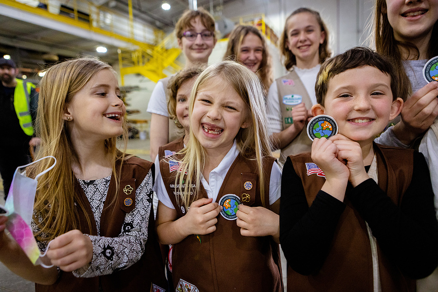A group of Girl Scouts are smiling and wearing their Girl Scout outfits and holding up the badge they just got. 