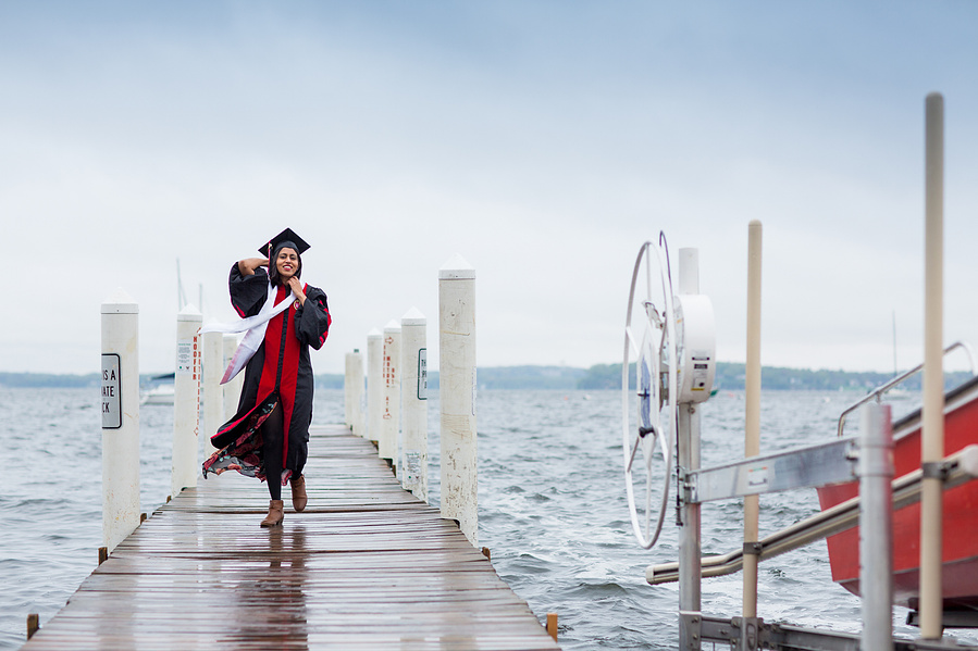 A UW Madison graduate is walking down the dock at the Memorial Union posing for graduation photos. 