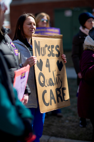 A women is holding a sign that says "Nurses 4 quality Care". She is at a protest to demand better rights for nurses. 
