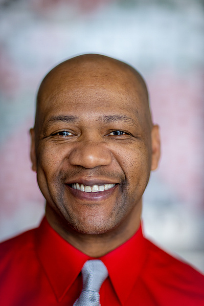 A bald man wears a red shirt. He has a real nice smile. 