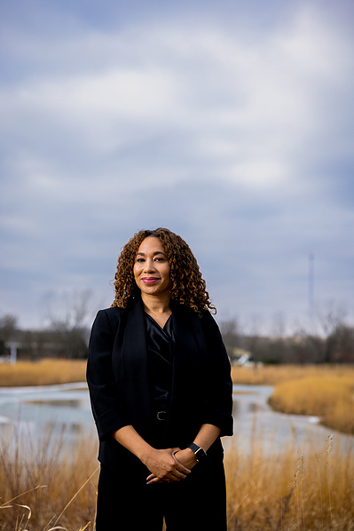 A women is standing in front of a field & holding her hands together. 