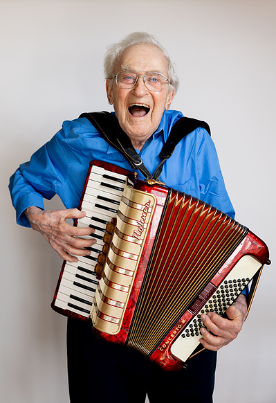 An older man is laughing and playing an accordion .