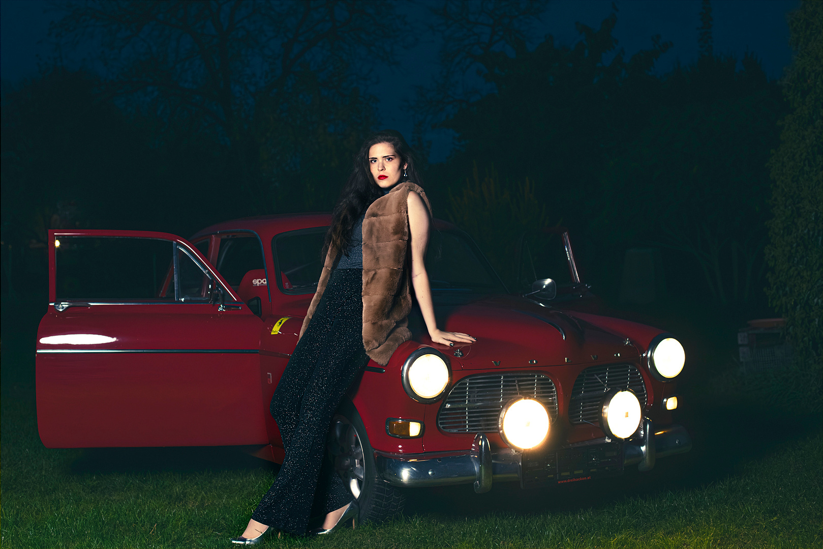 Stylisches Mode-Fotoshooting bei Nacht: Mädchen posiert auf rotem Oldtimer Volvo – urbaner Retro-Look mit besonderer Atmosphäre. Niederösterreich, Tulln, Krems an der Donau