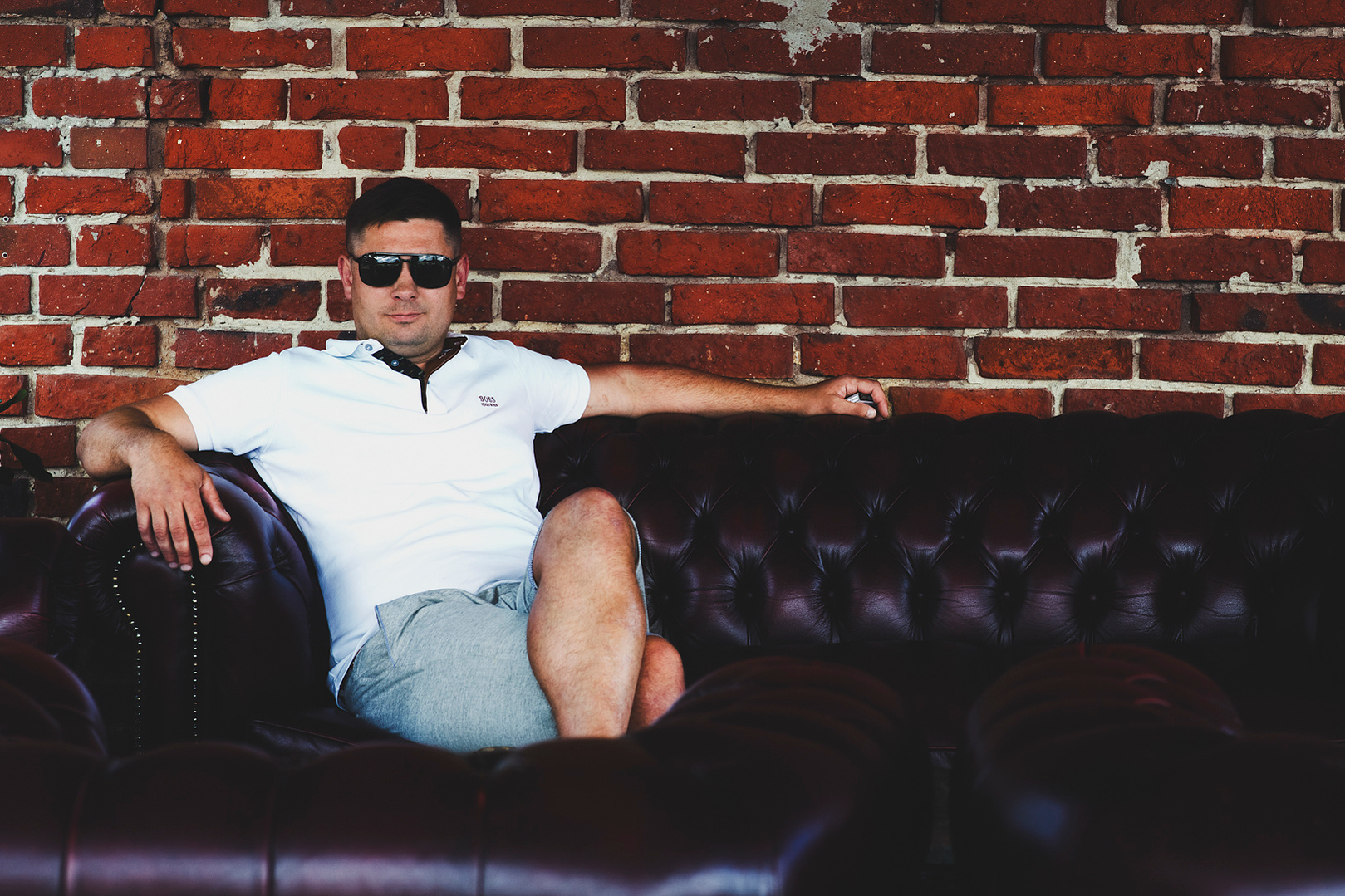 Stilvoller Mann auf einem Ledersofa vor einer Ziegelmauer – maskuline Portraitfotografie mit urbanem Flair. Niederösterreich, Tulln, Krems an der Donau