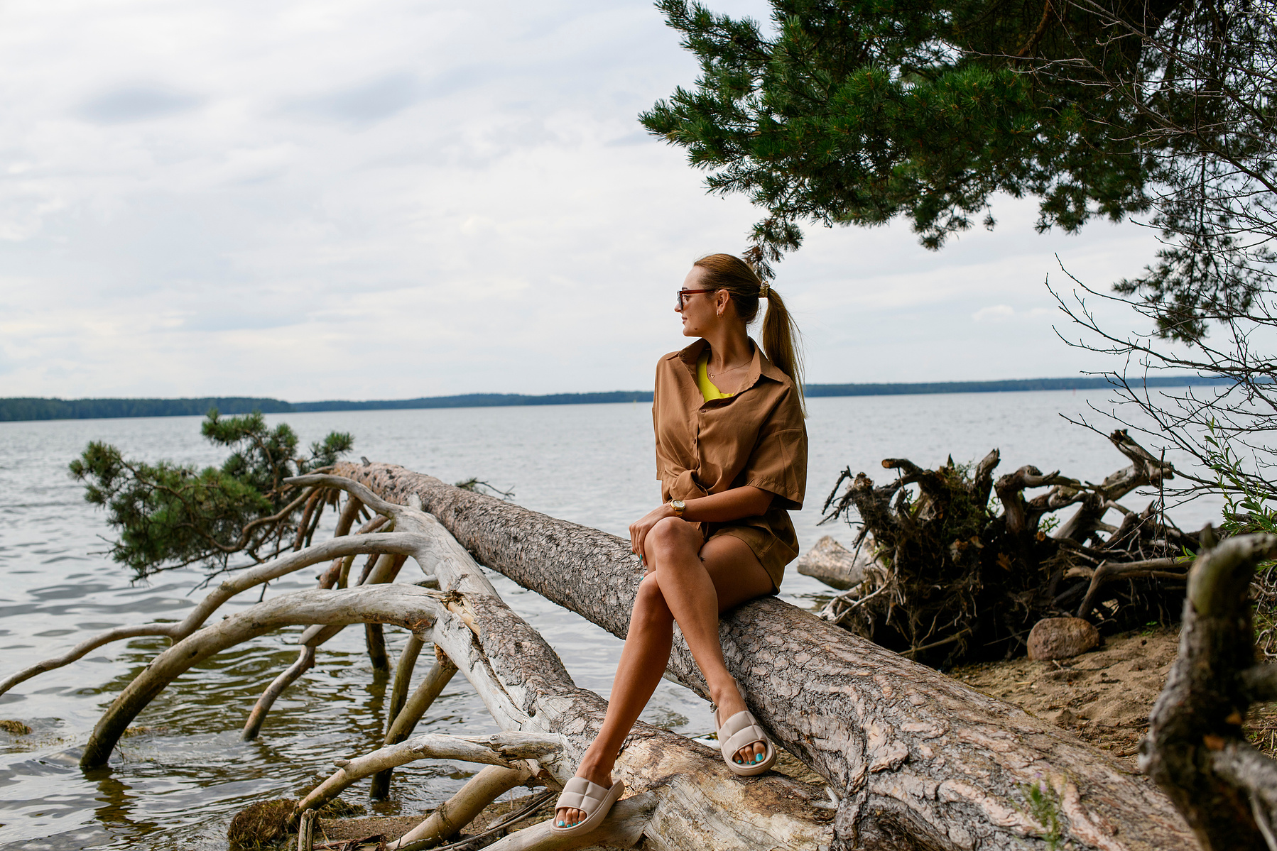 Mädchen sitzt entspannt auf einem Baum am See – natürliche und friedliche Outdoor-Fotografie voller Abenteuerlust. Niederösterreich, Tulln, Krems an der Donau