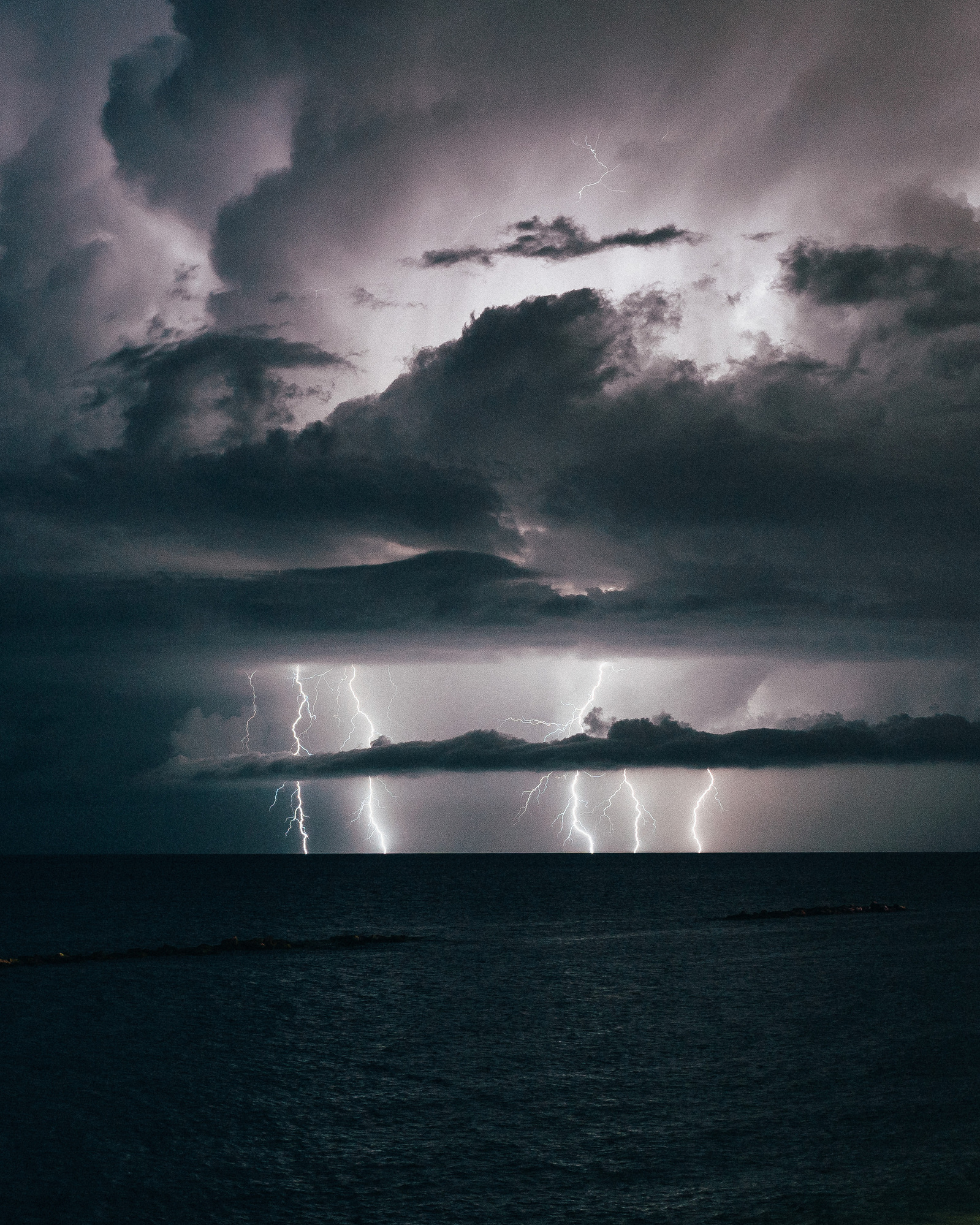 Landscape photo of lightning bolts on sea at night during a storm with clouds
