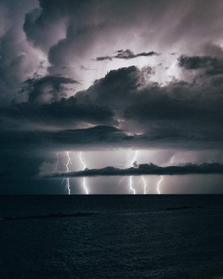 Landscape photo of lightning bolts on sea at night during a storm with clouds
