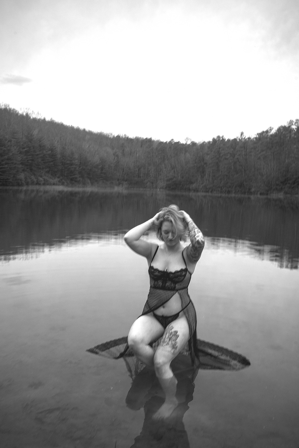 Woman seated on a stool in the middle of a lake during an outdoor boudoir photography session at a lake in DuPont Forest near Asheville, NC