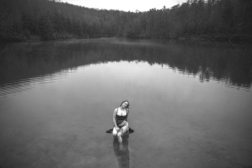 Woman seated on a stool in the middle of a lake during an outdoor boudoir photography session at a lake in DuPont Forest near Asheville, NC