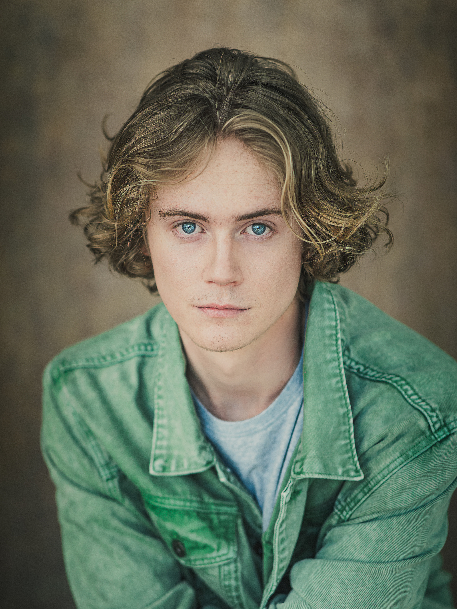 Headshot of a male actor wearing a green jacket against a brown background