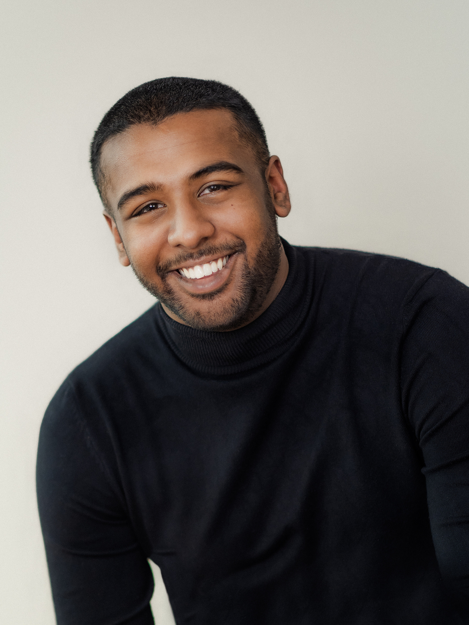 Headshot of a male actor wearing a black skivvy against a pale background