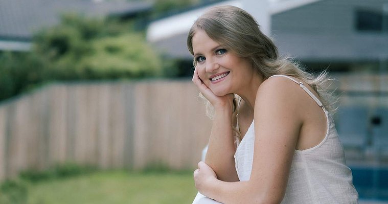 Dating profile photo of a single woman smiling and leaning on a deck balcony railing.