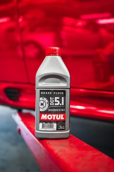 Motul DOT 5.1 brake fluid product shot next to a modified MINI Cooper R56 