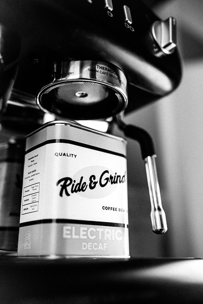 A low angle photograph of a coffee tin placed on a coffee espresso machine. The tin has the brands logo on the front which reads "Ride & Grind" a Coffee roasters based in Edinburgh.  